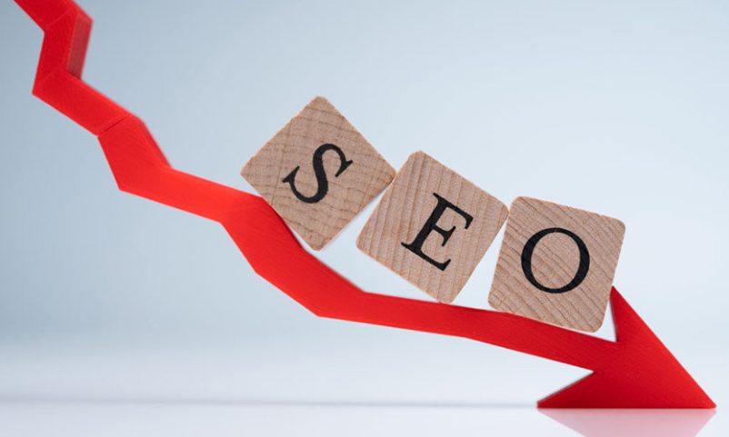 A wood block of SEO above a red arrow going down