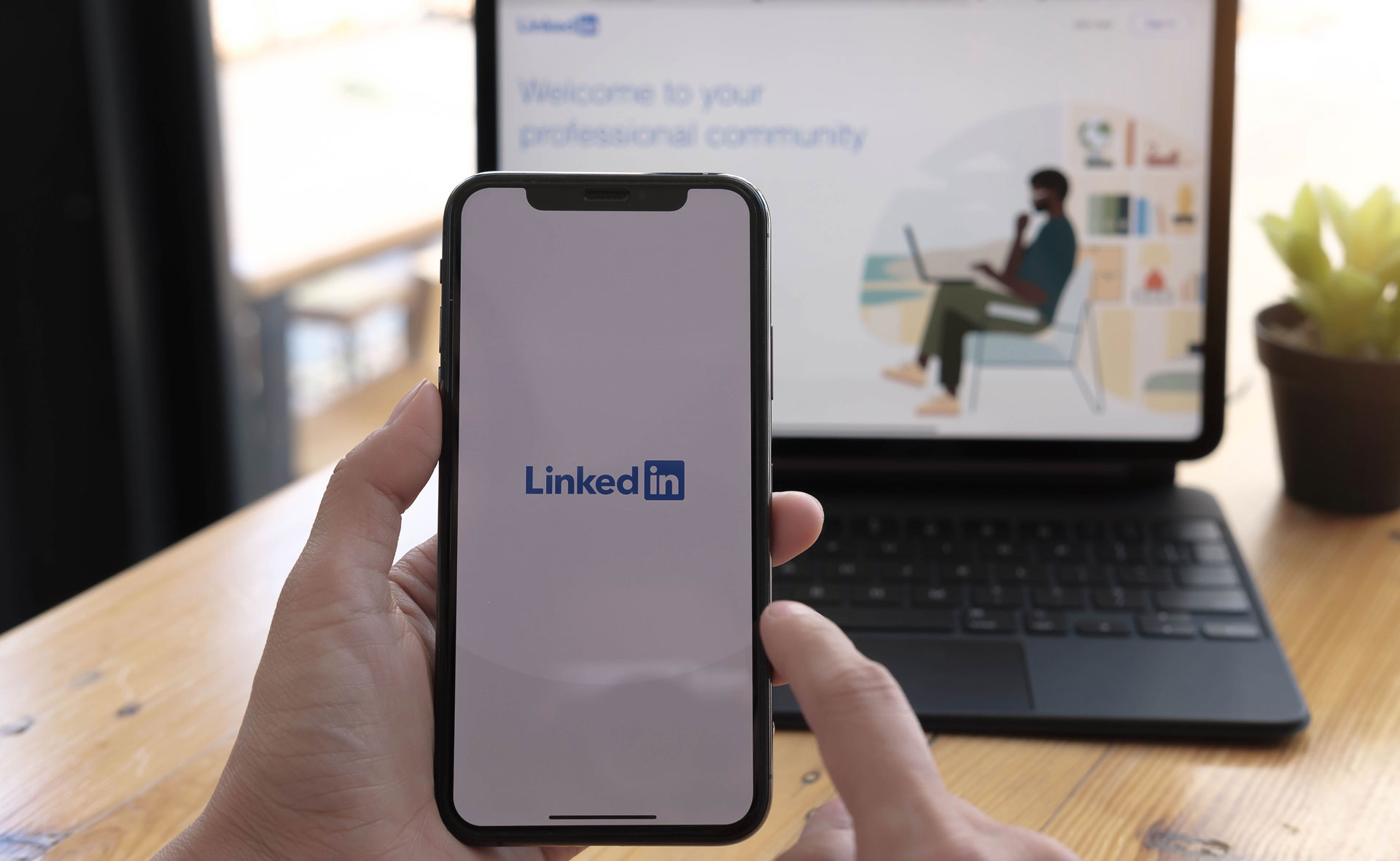 man holding a phone with linkedin loading page in front of a laptop