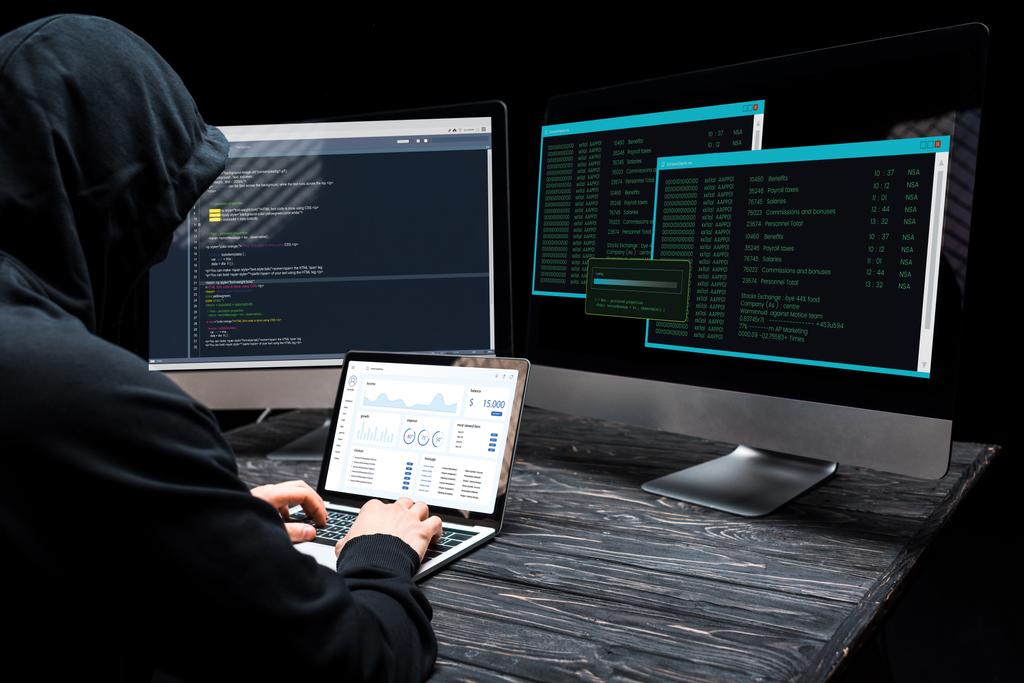 man in black hoodie using laptop with graphs and charts in the multiple screens